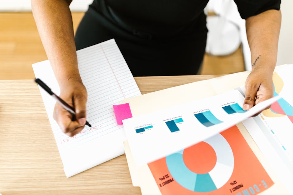 Businesswoman writing notes while analyzing printed graph reports at a desk.